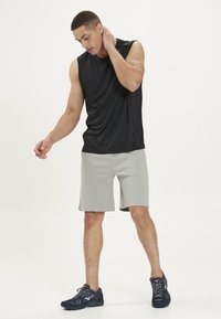 Sort ærmeløs trænings skjorte, grå shorts og mørke løbesko. Glat stof, afslappet pasform og knæ-lange shorts med sidelommer.