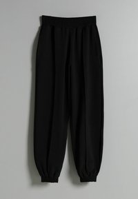 Svarta joggerbyxor med elastisk midja, sidofickor och elastiska mudd vid anklarna, tillverkade av ett mjukt och lätt material.