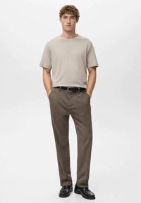 Beige bomuld t-shirt med løs pasform, kombineret med brune bukser med en glat tekstur. Sorte lædersko fuldender looket.