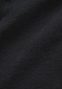 Tissu noir foncé avec un motif losange tissé subtil et une texture visible, présentant de doux plis et des ombres.