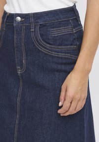 Jeanskjol i mörk tvätt med synliga sömnadsdetaljer, framfickor, rak passform och knappstängning i midjan.