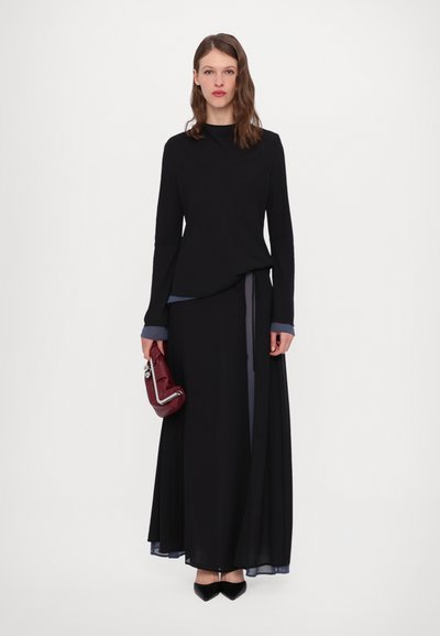 Black long-sleeve top layered over a floor-length black skirt, featuring light blue accents on cuffs and a tied belt. Burgundy handbag, black shoes.