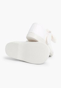 Weiße Leinenschuhe mit einer weichen Sohle, die mit einer Schleifenakzent versehen sind. Das Design ist niedrig geschnitten, mit einer glatten, strukturierten Laufsohle für besseren Halt.