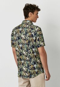 Korte mouw shirt in donker marineblauw, met een bloemenpatroon van groene en witte bladeren, ontspannen pasvorm en kraagontwerp.