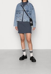 Jeansjacka i ljusblått, kort design; ribbad svartgrå klänning med vågig nederdel; svarta loafers; randiga strumpor.