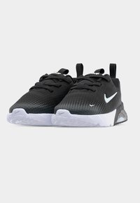 Ζευγάρι μαύρα και λευκά αθλητικά παπούτσια Nike με πουά μοτίβο, σχεδιασμό με κορδόνια και θηλιές σε απλό ανοιχτό γκρι φόντο.