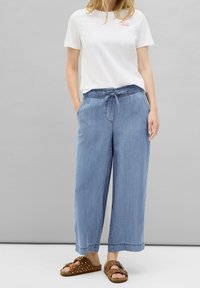 Jasnoniebieskie spodnie szerokie z elastyczną talią i sznurkiem. Połączone z prostą białą koszulką i brązowymi sandałami z ćwiekami.