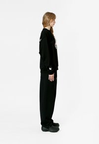 Sudadera negra de gran tamaño con gráfico. Pantalones de chándal negros con un bolsillo lateral. Calzado negro grueso con parte superior texturizada.