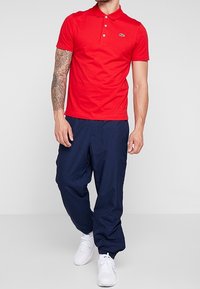 Červené bavlněné polo tričko s tříknopovou légou a malým značkovým logem. Kombinováno s námořnicky modrými zúženými tepláky a bílými teniskami.