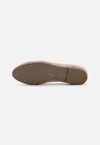 Chaussure rose clair avec une tige douce semblable au daim. La semelle en caoutchouc présente une texture à motifs et une forme de bout arrondi, conçue pour le confort.