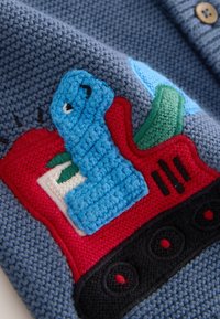 Pull bleu tricoté avec un patch crochet coloré représentant un train, comprenant une locomotive bleue, une carrosserie rouge, une feuille verte et des roues noires.