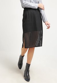 Svart midikjol med en strukturerad, ribbad design, med sidslitsar för rörelse. Kombinerad med svarta ankelstövlar och en silverfärgad topp.