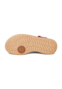 Sole of a shoe, featuring a textured light brown rubber surface with parallel grooves, a round logo, and a pink strap accent.