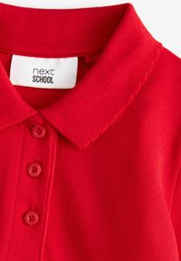 Czerwona koszulka polo z kołnierzykiem, trzema guzikami oraz teksturowaną tkaniną. Metka mówi "next SCHOOL."