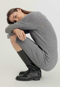 Abito grigio lavorato a maglia con maniche lunghe, dalla silhouette aderente. Indossato con stivali neri in pelle alta fino al ginocchio con suola testurizzata.