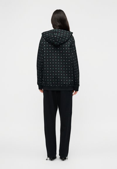 Μαύρο φούτερ με κουκούλα και πράσινο σχέδιο, διαθέτει κουκούλα, ριμπ μανσέτες και άνετη γραμμή, συνδυασμένο με μαύρο παντελόνι με φερμουάρ.