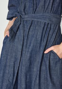 Abito in denim con cintura legata, colore blu scuro, tessuto testurizzato, con vita arricciata e tasche laterali.