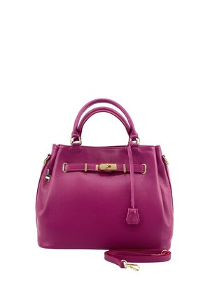 Lila Lederhandtasche mit doppeltem Griff, goldenem Verschluss, hängendem Lederetikett und abnehmbarem Schulterriemen vor weißem Hintergrund.
