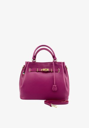 Lila Lederhandtasche mit doppeltem Griff, goldenem Verschluss, hängendem Lederetikett und abnehmbarem Schulterriemen vor weißem Hintergrund.