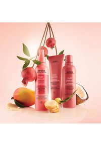 Tre Aveda Nutri Plentish hårvårdsprodukter i rosa flaskor: schampo, balsam och leave-in balsam. Omgivna av frukter och kokos.