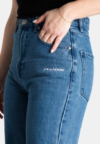 Blauwe denim high-waisted jeans met een rechte pasvorm. Kenmerkt zich door een geborduurd logo "PEGADOP" op de dij en een klassiek vijf-pocket ontwerp.