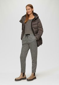 Dunkelgraue Steppjacke mit Kapuze, graues langärmliges Oberteil, gemusterte graue Sweatpants und braune Stiefeletten mit schwarzen Akzenten.