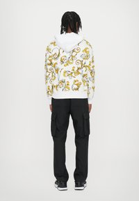 Hooded sweatshirt in white with black and yellow floral pattern, paired with black cargo pants. Sweatshirt features ribbed cuffs and hem.