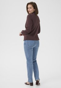 Bordový blazer s vysokým límcem, přiléhavým střihem a bílými akcenty, kombinovaný s světle modrými kalhotami rovného střihu a tmavě hnědými lodičkami na podpatku.