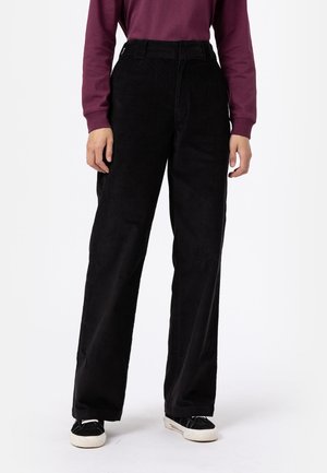 Pantaloni a coste neri con vita alta, taglio dritto e texture sottile. Indossati con una camicia a maniche lunghe color bordeaux e sneakers nere.