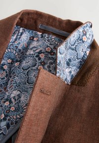 Brauner Blazer aus strukturiertem Stoff mit einem gemusterten blauen Blumenfutter. Verfügt über einen Reverskragen und sichtbare Nähdetails.