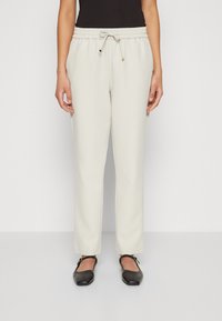Lys beige joggebukser med elastisk midjebånd og snøring, med en glatt tekstur og innsvingt passform, sammen med svarte leiligheter.