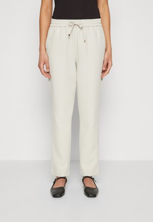 Lys beige joggebukser med elastisk midjebånd og snøring, med en glatt tekstur og innsvingt passform, sammen med svarte leiligheter.