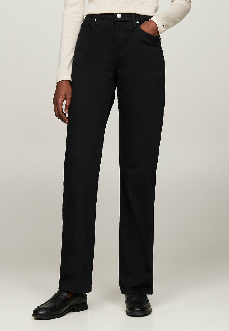 Jeans noirs à jambes droites en denim avec une texture lisse. Présentent des poches avant, une fermeture éclair et des accents en métal sur le bouton.