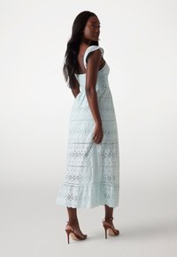 Light blue, embroidered maxi dress with lace accents, fitted bodice, flared hem, and shoulder straps. Worn with brown high-heeled sandals.