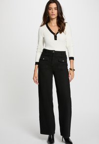 Pantalones de pierna ancha negros con bolsillos delanteros, combinados con una blusa blanca de canalé con cuello en V negro y detalles de botones. Textura de tela suave.