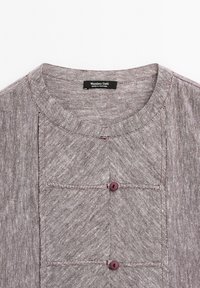 Graues, strukturiertes Oberteil mit rundem Halsauschnitt, das über zwei kastanienbraune Knöpfe und ein rechteckiges Taschendesign verfügt. Marke: Massimo Dutti. Hergestellt in Portugal.