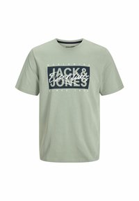 Camiseta de algodón verde claro con mangas cortas. Presenta un gráfico rectangular azul marino con el texto "JACK & JONES" en blanco, escrito y impreso a mano.