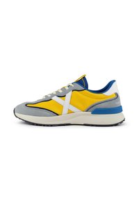Baskets de sport avec une tige en mesh jaune prédominant, des accents en suède gris, des coutures blanches et un contrefort de talon bleu.