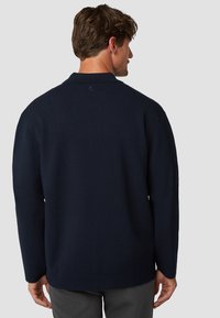 Marineblauwe gebreide trui met een comfortabele pasvorm, geribde manchetten en zoom. Bevat een subtiel logo detail nabij de kraag.