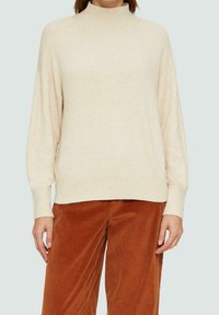 Pull à col roulé couleur crème avec une coupe décontractée, épaules tombantes, col et ourlet côtelés, fabriqué en tissu doux et texturé.