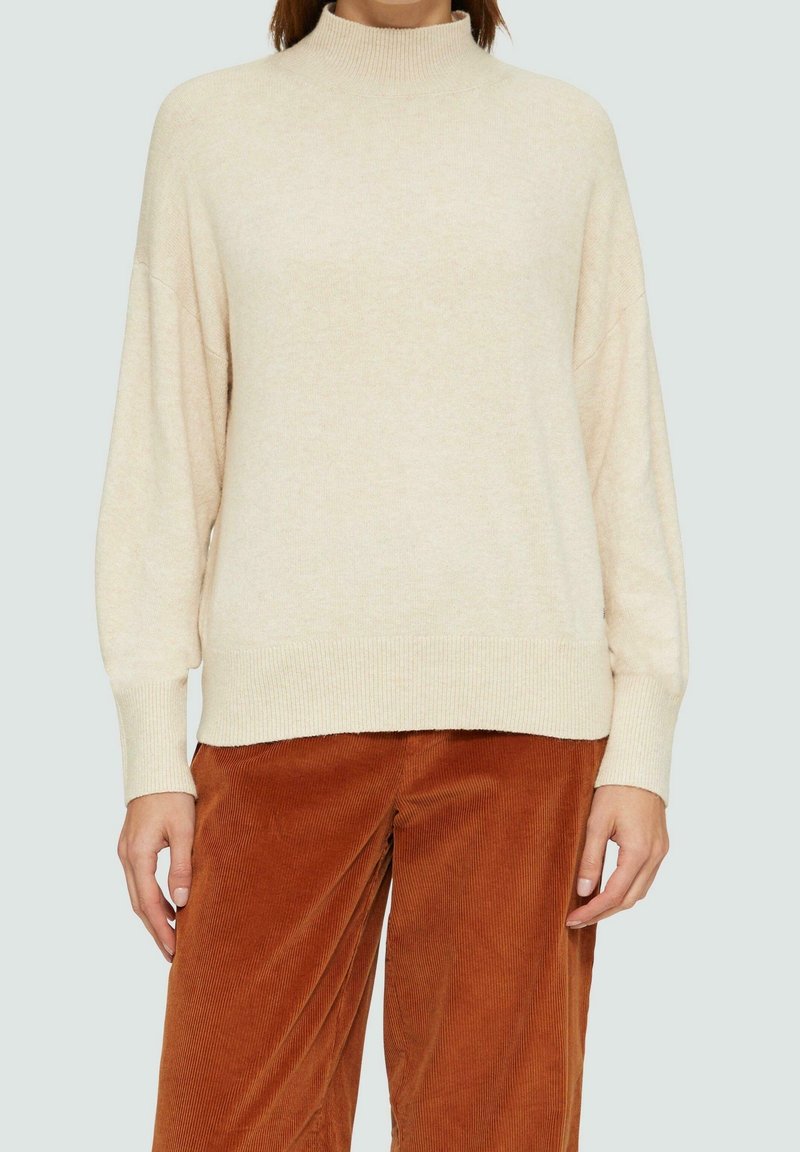 Pull à col roulé couleur crème avec une coupe décontractée, épaules tombantes, col et ourlet côtelés, fabriqué en tissu doux et texturé.