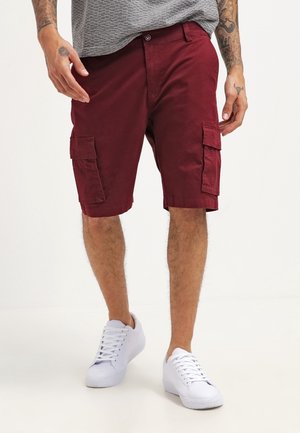 Bordeauxroter Cargo-Shorts mit Seitentaschen, aus Baumwollmischgewebe. Kombiniert mit weißen Sneakers und einem grau strukturierten Hemd.