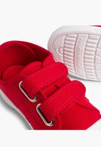 Zapatos de lona rojos con dos correas de velcro, suelas de goma blanca y detalles de costura. El forro interior también es rojo, lo que proporciona un aspecto coherente.