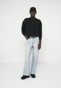 Černá mikina, světle modré volné džíny, vzorovaný pásek, černé boty, černá kšiltovka; hladká textury, volný střih, neformální styl.