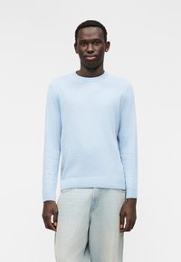Pull bleu clair  à col rond avec manches longues, texture fine et ourlet côtelé. Porté avec un jean délavé clair et ample.