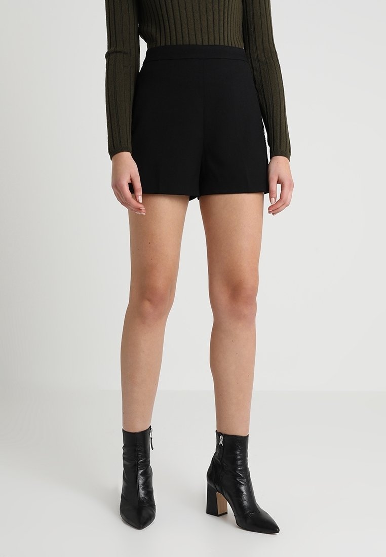 Svarta shorts med skräddarsydd design och slätt tyg, i kombination med svarta läder ankle boots med dragkedja och klackar.