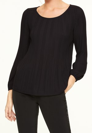 Maglia nera a maniche lunghe con texture a coste, scollatura rotonda e polsini elasticizzati. Il tessuto è leggermente trasparente, abbinato a pantaloni neri.