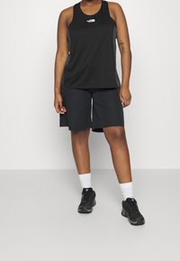 Zwarte sport tanktop met horizontale strepen, gecombineerd met zwarte shorts. Zwarte schoenen en witte sokken maken de outfit compleet.