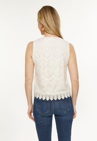 Kermanitön, kukkakuosis lace-top vaaleassa sävyssä, jossa on aallokkomuotoinen helma, yhdistetty tummansinihin tiukkoihin farkkuihin, joissa on takataskut.