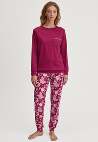 Langsleeve magenta top met een borstzak en witte accenten, gecombineerd met floral gemusterde magenta en witte broek, gemaakt van zachte stof.